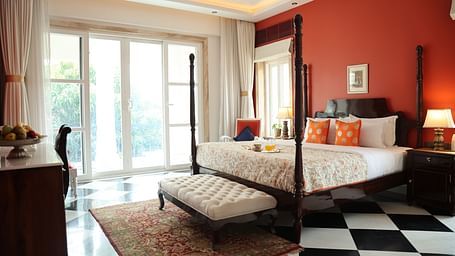 A room at Dileep Kothi, Jaipur with a double bed, side tables with night lamps, French windows, and chequered tiles